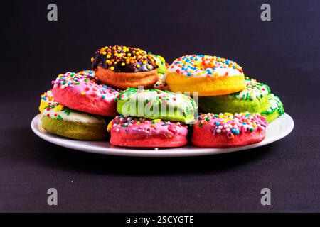 Bunte Donuts auf einer weißen Platte auf schwarzem Hintergrund Stockfoto