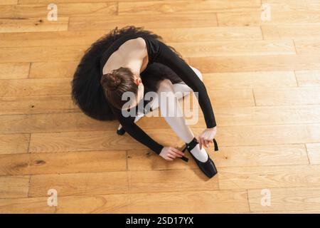 Die Ballerina zieht im Tanzkurs spitzenschuhe an. Klassische Balletttänzerin im Tanzstudio. Ballerina, die klassische spitzenschuhe für Tanztraining anzieht. Ballettschulkonzept Stockfoto