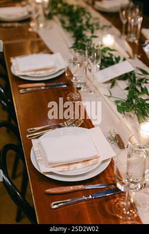 Ein schön gestalteter Esstisch mit Tellern, Besteck und Grün, bereit für eine besondere Veranstaltung. Stockfoto