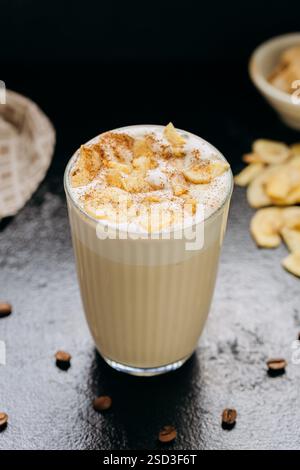 Cremiger Latte mit geschlagenem Schaum, getrockneten Apfelscheiben und Zimt, serviert auf einer dunklen strukturierten Oberfläche Stockfoto