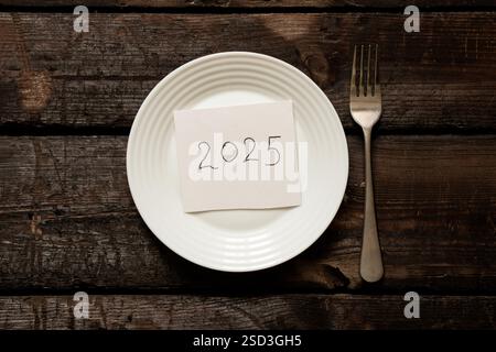 2025 auf Papier geschrieben, auf einem Teller auf einem alten Holzbrett liegend Stockfoto