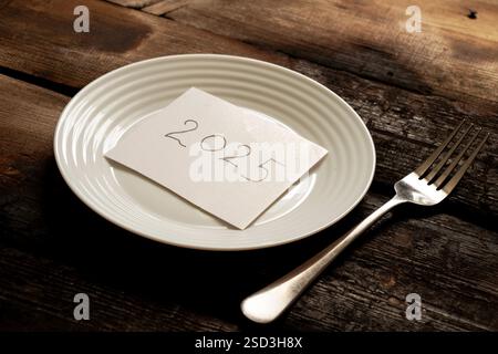 2025 auf Papier geschrieben, auf einem Teller auf einem alten Holzbrett liegend Stockfoto