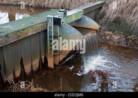 Kleiner Überlaufdamm mit Wasserstandsanzeige in einem Fluss zur Kontrolle des Wasserspiegels in einem Naturschutzgebiet Stockfoto