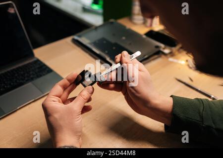 Nahaufnahme der Techniker-Hände, die die Smartwatch-Batterie sorgfältig mit einer Pinzette austauschen, um den komplizierten Prozess der Reparatur elektronischer Geräte zu demonstrieren Stockfoto