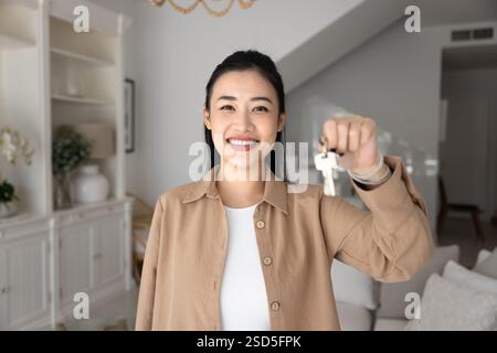 Positiv zufriedene junge asiatische neue Hausbesitzerin, die Schlüssel zeigt Stockfoto