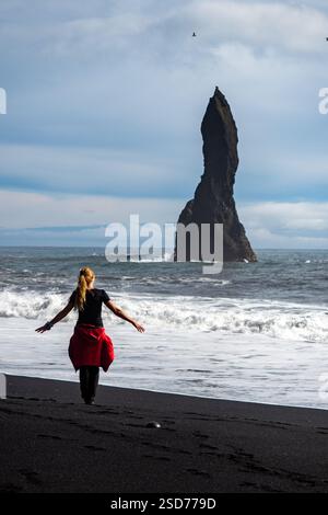 Eine Person, die entlang eines atemberaubenden schwarzen Sandstrandes Reynisfjara in Island in VIK Myrdal im Golden Circle Gebiet spaziert, mit Wellen des Atlantischen Ozeans Stockfoto