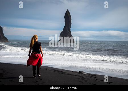 Eine Person, die entlang eines atemberaubenden schwarzen Sandstrandes Reynisfjara in Island in VIK Myrdal im Golden Circle Gebiet spaziert, mit Wellen des Atlantischen Ozeans Stockfoto