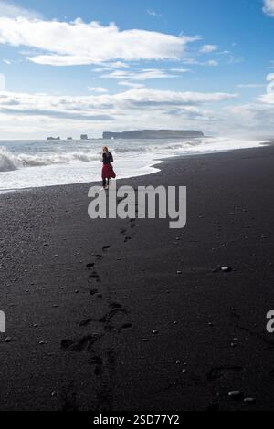 Eine Person, die entlang eines atemberaubenden schwarzen Sandstrandes Reynisfjara in Island in VIK Myrdal im Golden Circle Gebiet spaziert, mit Wellen des Atlantischen Ozeans Stockfoto