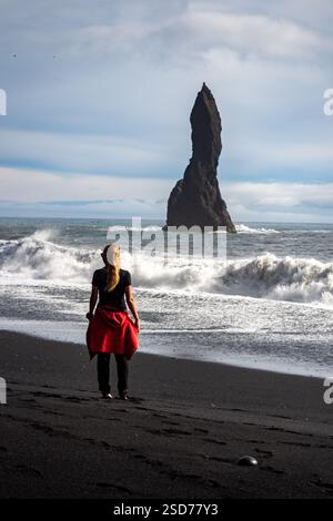 Eine Person, die entlang eines atemberaubenden schwarzen Sandstrandes Reynisfjara in Island in VIK Myrdal im Golden Circle Gebiet spaziert, mit Wellen des Atlantischen Ozeans Stockfoto