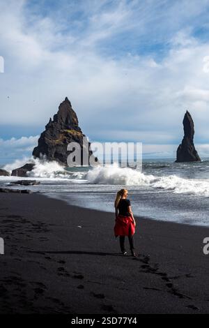 Eine Person, die entlang eines atemberaubenden schwarzen Sandstrandes Reynisfjara in Island in VIK Myrdal im Golden Circle Gebiet spaziert, mit Wellen des Atlantischen Ozeans Stockfoto