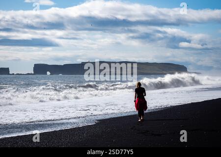 Eine Person, die entlang eines atemberaubenden schwarzen Sandstrandes Reynisfjara in Island in VIK Myrdal im Golden Circle Gebiet spaziert, mit Wellen des Atlantischen Ozeans Stockfoto
