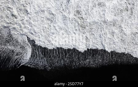Fesselnder Blick auf die Meereswellen an einem schwarzen Strand von reynisfjara, der weißen Schaum bildet, während sie auf eine dunkle Sandküste stürzen und die Be zeigen Stockfoto