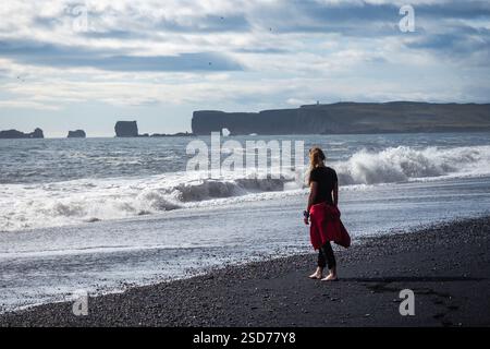 Eine Person, die entlang eines atemberaubenden schwarzen Sandstrandes Reynisfjara in Island in VIK Myrdal im Golden Circle Gebiet spaziert, mit Wellen des Atlantischen Ozeans Stockfoto