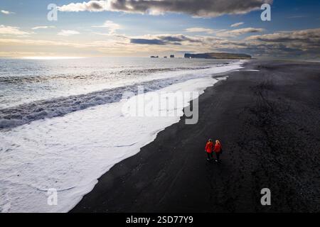 Aerail View Pärchen, die entlang eines atemberaubenden schwarzen Sandstrandes Reynisfjara laufen, Sonnenuntergang in Island VIK Myrdal in Golden Circle Gegend mit Atlantik Waves Stockfoto