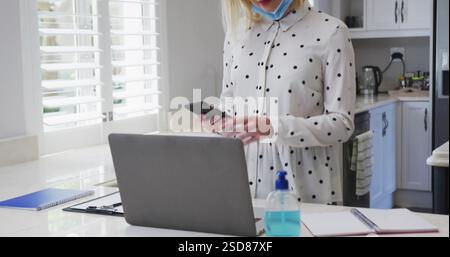 Bild einer Frau im Polka Dot Shirt mit Smartphone und Laptop in der modernen Küche Stockfoto