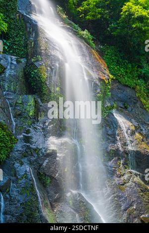 Wasserfall, der eine Rocky Cliff mit einem Regenbogen hinunterstürzt Stockfoto