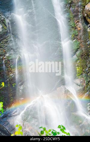 Wasserfall, der eine Rocky Cliff mit einem Regenbogen hinunterstürzt Stockfoto