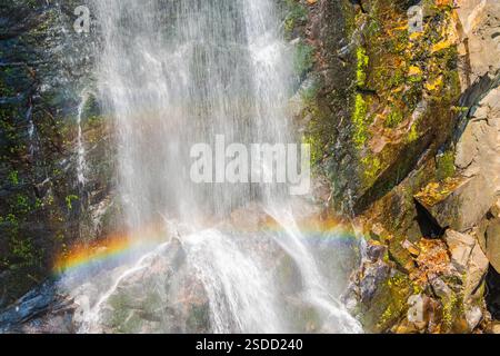 Wasserfall, der eine Rocky Cliff mit einem Regenbogen hinunterstürzt Stockfoto