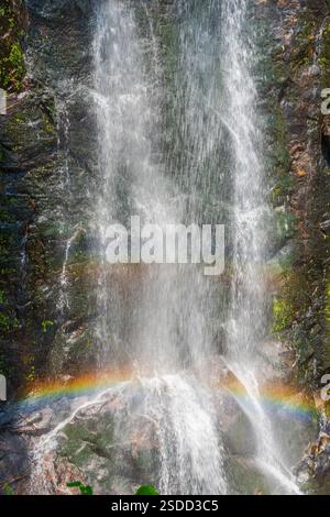 Wasserfall, der eine Rocky Cliff mit einem Regenbogen hinunterstürzt Stockfoto