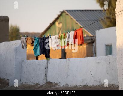 Farbenfrohe, frisch gewaschene Kinderkleidung hängt an einer Wäscheleine in einem ländlichen Dorf in Usbekistan. Stockfoto