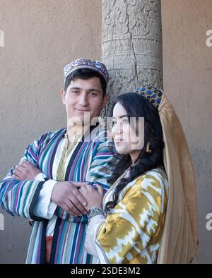 Das lächelnde junge usbekische Paar mit traditioneller Kleidung aus Ikat-Stoff posiert für ein Porträt eines anderen Fotografen. Stockfoto