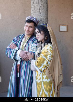 Das junge usbekische Paar mit traditionellen Kleidungsstücken und Kopfbedeckungen posiert für ein Foto auf der Zitadelle, die die Altstadt von Chiwa in Usbekistan umgibt. Stockfoto