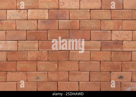 Eine rustikale rote Ziegelwand mit verwitterter Textur, die Erdtöne und natürliche Mängel für einen industriellen Look zeigt. Stockfoto