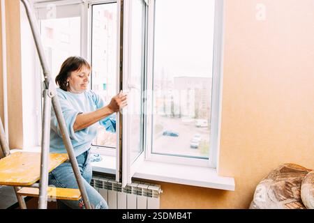 Glückliche Schüchterne, Fröhlich Lächelnde Reife Frau, Die Das Fenster Reinigt. Kaukasische Frau Im Mittleren Alter. Active Seniors-Konzept. Reinigungsappartement Für Ältere Frauen Stockfoto