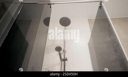 Chrom-Duschkopf mit Handsprühgerät für elegantes Design, moderne Badeinrichtung mit minimalistischen weißen Fliesen und sauberer Architektur Stockfoto