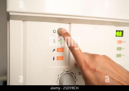 Zugeschnittene Ansicht der Hand eines Mannes, der einen Knopf auf dem Heizkessel mit heißem Wasser drückt Stockfoto