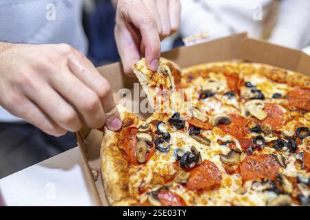 Hände greifen Scheiben von einer Pizza mit verschiedenen Belägen, einschließlich Pfefferoni Stockfoto