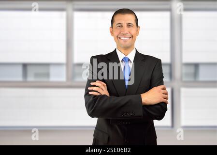 Abgeschnittenes Porträt eines Geschäftsmannes, der mit gefalteten Armen in seinem Büro steht Stockfoto