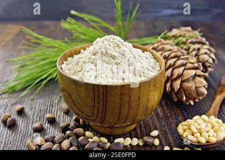 Mehl Zedernholz in einer Holzschale, Zedernnüsse und zwei Kegel, ein Löffel mit geschälten Nüssen, Zedernzweig vor dem Hintergrund von Holzdielen Stockfoto