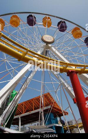 Sonniger Tag am Santa Monica Pier mit einer Kombination aus einem riesigen Riesenrad und einer Achterbahn über dem Ozean, die eine lebhafte Szene im Vergnügungspark schafft Stockfoto