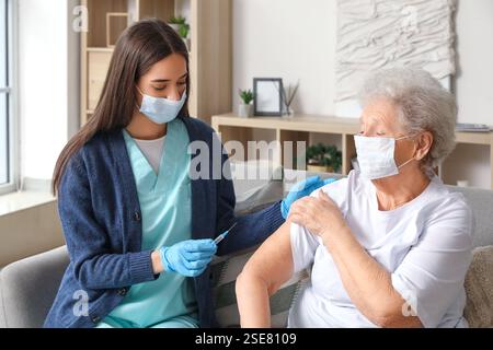 Junge Krankenschwester geimpft Seniorinnen zu Hause Stockfoto