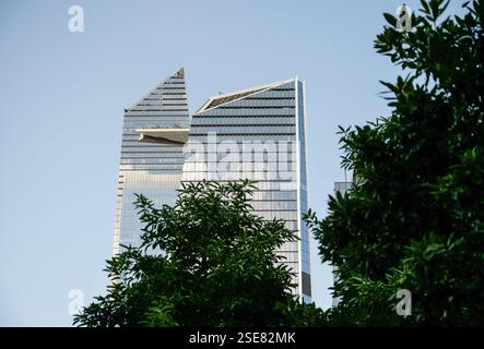 Hohe, moderne Wolkenkratzer mit einzigartigen architektonischen Designs stehen vor einem hellblauen Himmel. Grüne Bäume wetteifern um Aufmerksamkeit im for Stockfoto
