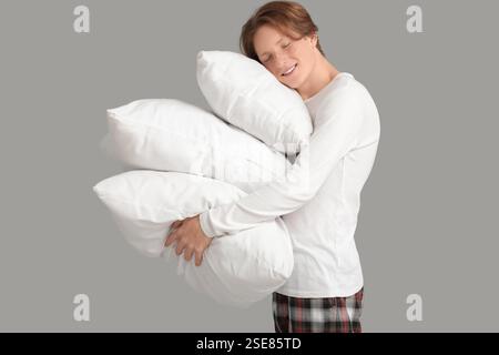 Hübscher junger glücklicher Mann im Pyjama mit Kissen, die auf grauem Hintergrund schlafen Stockfoto