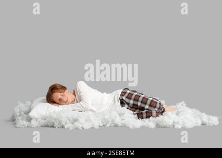 Schöner junger glücklicher Mann im Pyjama mit Kissen und Füllung, der auf grauem Hintergrund schläft Stockfoto