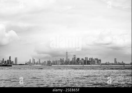 Vom Ufer aus ist eine entfernte Skyline der Stadt zu sehen, die von hohen Gebäuden unter einem stimmungsvollen Himmel dominiert wird. Wolken sammeln sich unheilvoll und verleihen dem Ur Tiefe Stockfoto