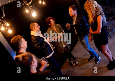 Enge Freunde, die sich in lebhaften Gesprächen unterhalten und Drinks während eines gemütlichen Abendessens, umgeben von warmer Beleuchtung, austauschen. Stockfoto