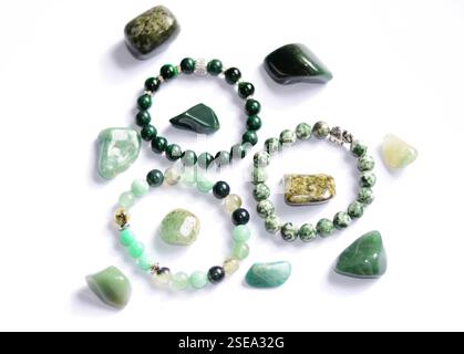 Eine atemberaubende Sammlung von verschiedenen grünen Rohmineralsteinen, kombiniert mit handgefertigten Armbändern, die natürliche Schönheit auf weißem Hintergrund zeigen Stockfoto