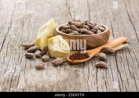 Kakaobutter oder Cocoa-Bohnen-Festöl mit Kakaopulver im Löffel und rohen Kakaobohnen in Holzschale auf rustikaler Kulisse, gesundes Naturöl Stockfoto