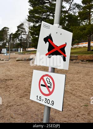 Ein Wegweiser in einem Sandstrand von Helsinki, Finnland, mit zwei Verbotsschildern: Eines, das anzeigt, dass Hunde nicht erlaubt sind, und ein anderes, das verboten ist Stockfoto