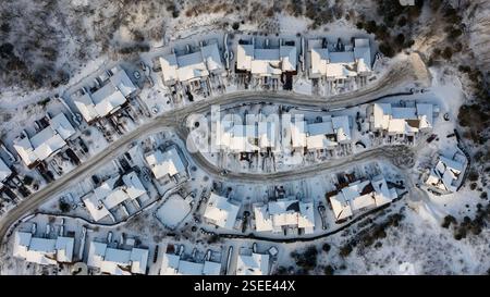 Ein Blick aus der Vogelperspektive zeigt eine kleine kanadische Stadt, die von frischem Schnee bedeckt ist. Die Dächer und Straßen glitzern weiß, während die Evergreens hoch stehen. Stockfoto