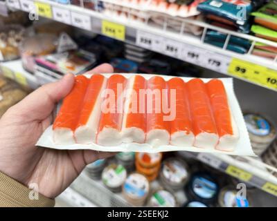 Kaukasische Hand hält verpackte nachgeahmte Krabbenstöcke im Lebensmittelgeschäft, Fisch- und Meeresfrüchtegang. Stockfoto
