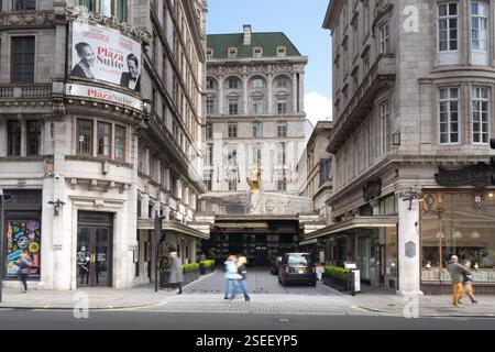Fußgänger gehen am Savoy Hotel, London, vorbei, mit einem großen Eingang und einer Statue. Ein Taxi steht vor dem Hotel. Stockfoto