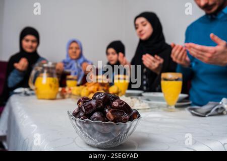 Glückliche muslimische Familie zusammen iftar dua zu brechen Fasten während des Ramadan am Esstisch zu Hause konzentrieren sich auf eine Schüssel Datteln gesunde Ernährung Stockfoto