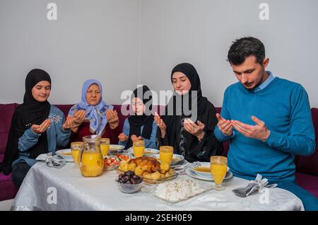 Muslimische Familie macht iftar dua zum Fastenbrechen während des Ramadan glückliche Eltern beim Abendessen mit ihren Kindern und Großmutter zu Hause am Esstisch Stockfoto