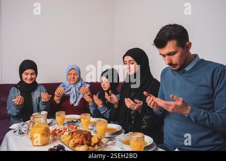Muslimische Familie macht iftar dua zum Fastenbrechen während des Ramadan glückliche Eltern beim Abendessen mit ihren Kindern und Großmutter zu Hause am Esstisch Stockfoto