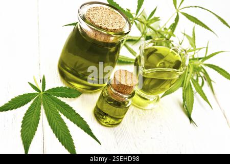 Hanf Öl in zwei Gläsern und sauceboat, Blätter und Stängel von Cannabis auf dem Hintergrund der Holzbretter Stockfoto